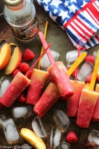 homemade popsicles laying on top of ice with raspberries and peaches