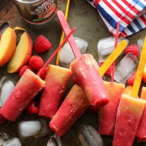 homemade popsicles laying on top of ice with raspberries and peaches