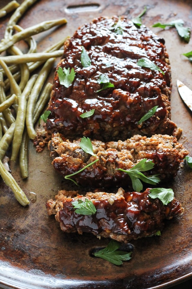 vegan meatloaf cut with 2 slices cut from the loaf next to green beans on a baking pan