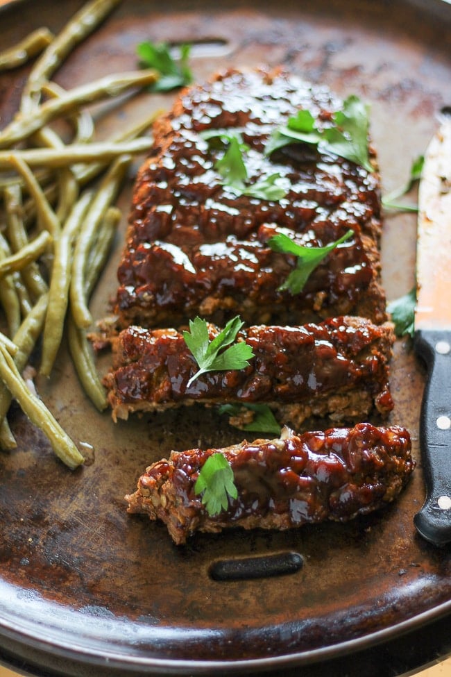 different angle of vegan meatloaf cut with 2 slices cut from the loaf next to green beans on a baking pan