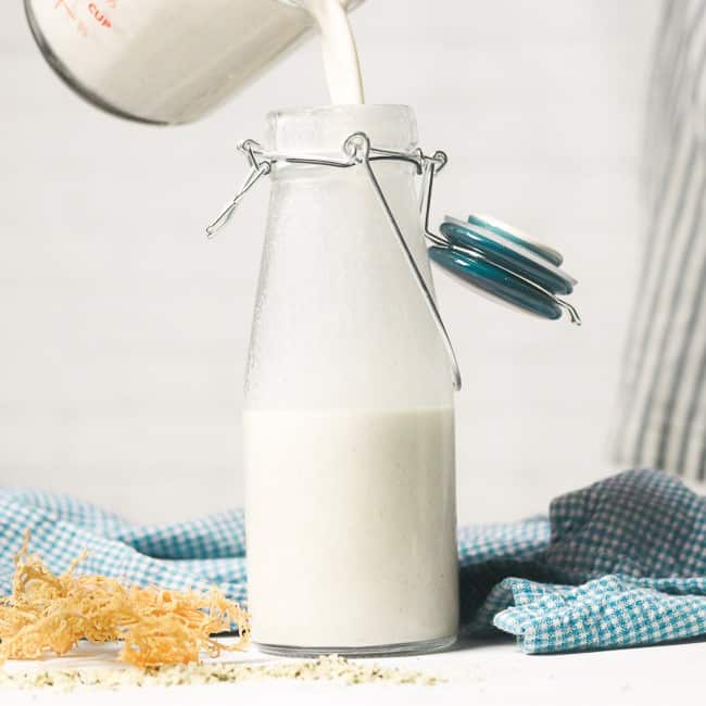 vegan milk being poured into a glass milk bottle