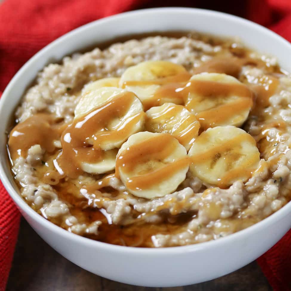 picture of oats topped with sliced bananas, maple syrup, and peanut butter in a white bowl