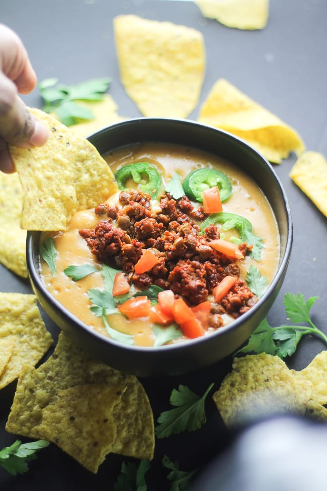 vegan nacho cheese sauce in a black bowl with a tortilla chip being dip in it