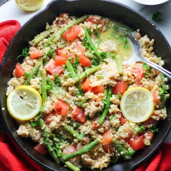 millet rice in cast iron skillet with veggies, lemon slices, and a spoon