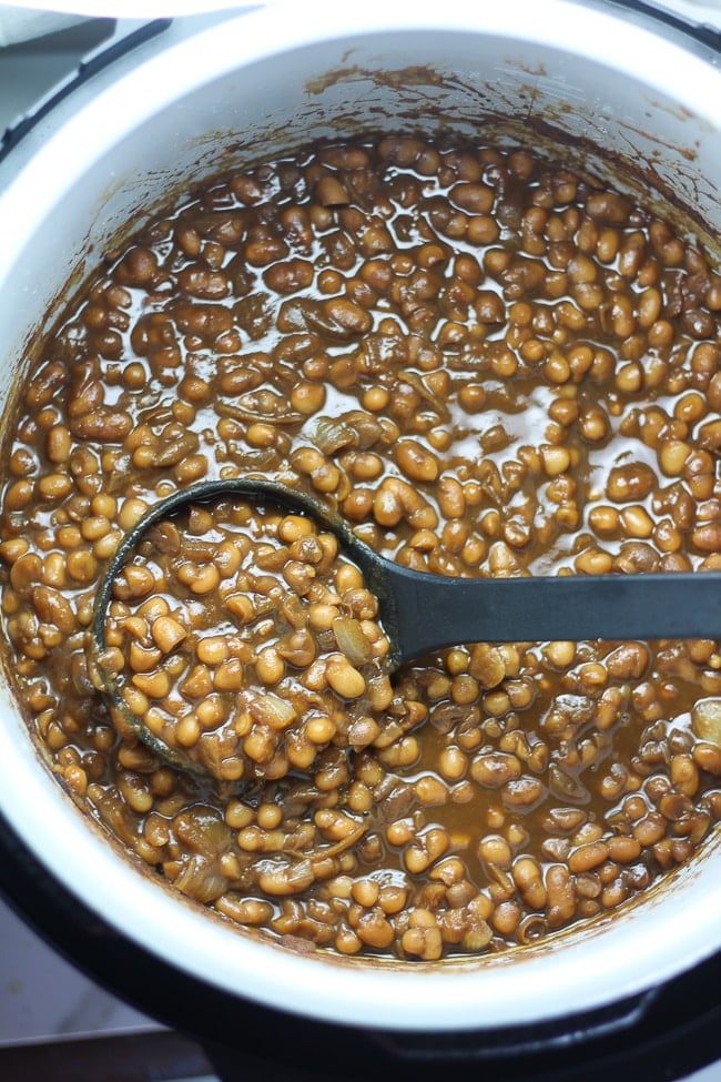 a picture of baked beans in a Ninja Foodi with a ladle scoping up beans