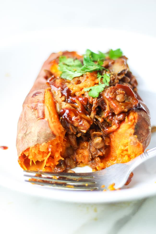 cut opened stuffed sweet potatoes on a plate with cilantro and bbq sauce with fork