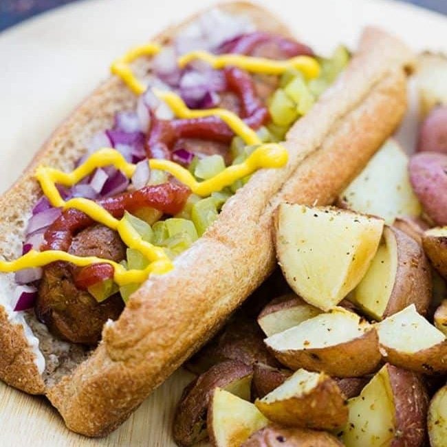 veggie hot dog on a bun with ketchup and onions with a side of potatoes
