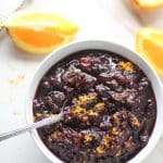 cranberry sauce in a white bowl with spoon in it next to sliced oranges