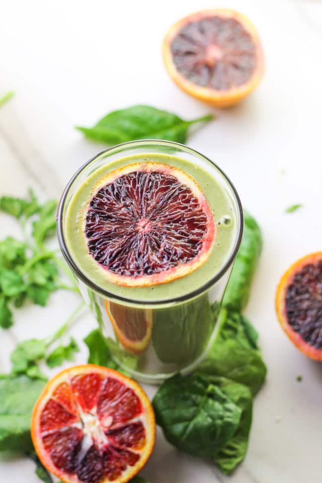 picture of blood orange smoothie in a glass with fresh spinach and blood orange slices around it