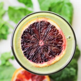 overhead shot of a green smoothie in glass with slice blood orange on top