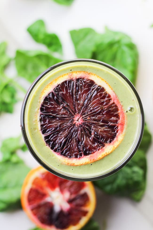 overhead shot of a green smoothie in glass with slice blood orange on top