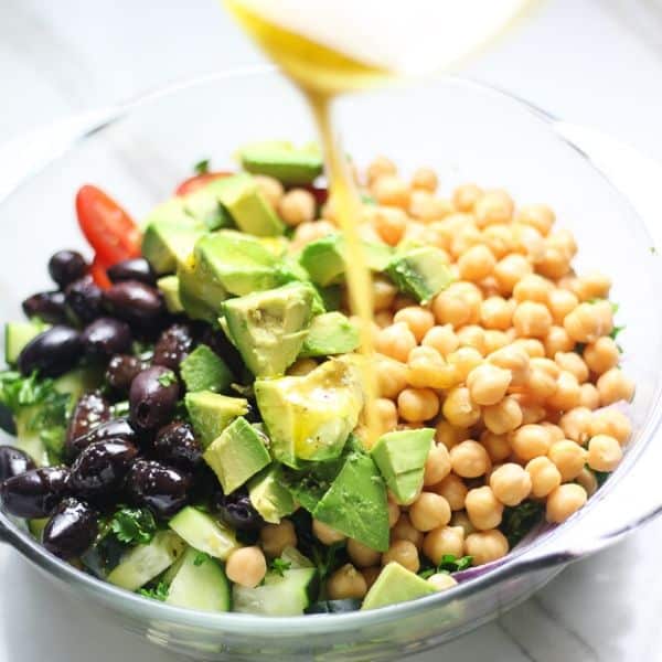 picture of salad with avocado, olives and oil dressing being poured