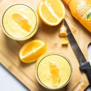 top angle of 2 glasses filled with orange smoothie with one orange slice on top