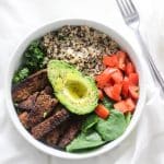 tempeh bacon, spinach, quinoa, kale tomatoes and half of avocado slice in a white bow with fork