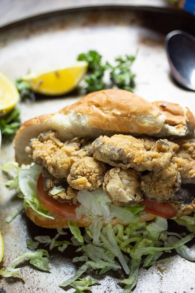 fried oyster mushrooms sandwich with french bread topped with lettuce and tomatoes with lemon slice