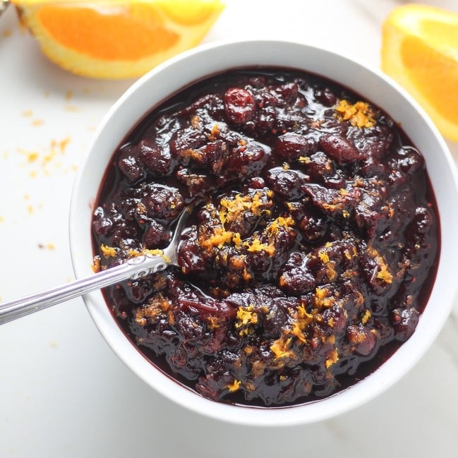 cranberry sauce in a white bowl with spoon in it next to sliced oranges