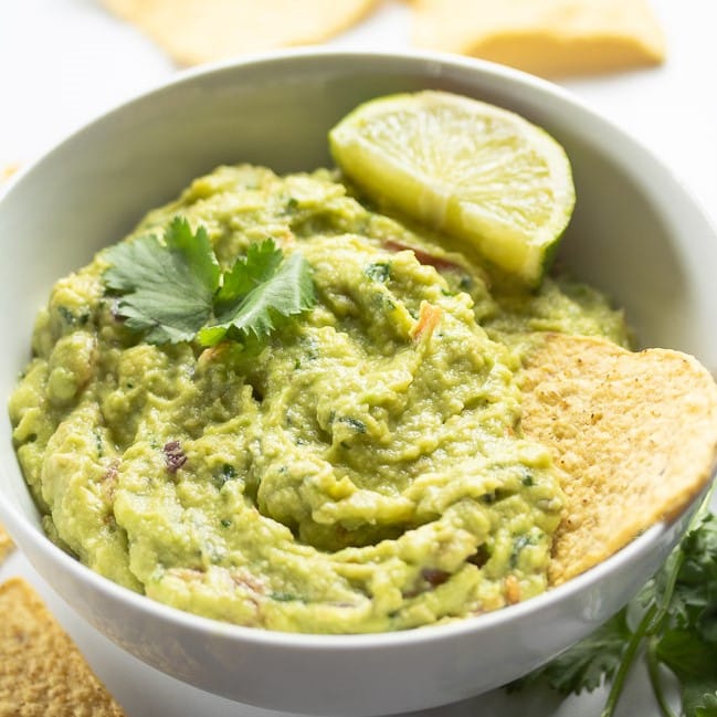 guacamole in a white bowl with tortilla chip and lime slice