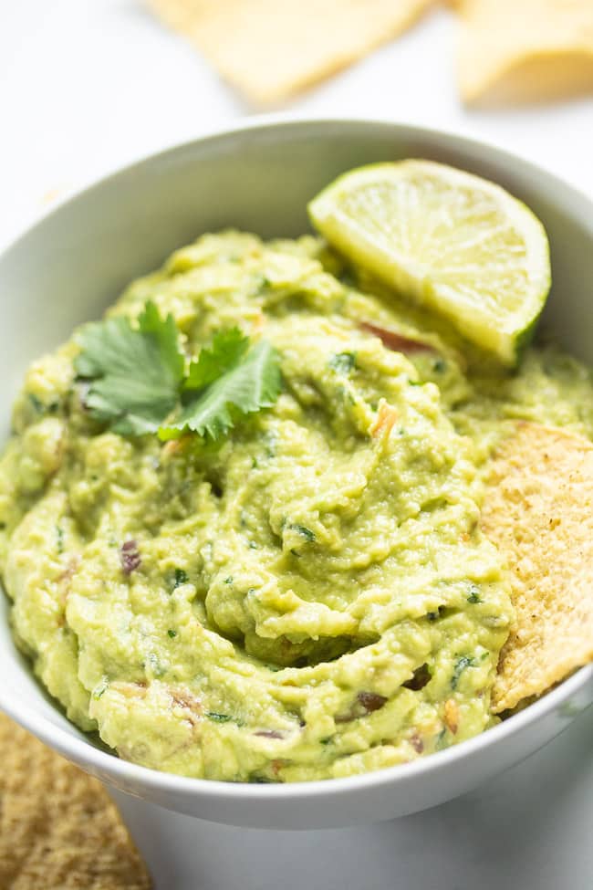 guacamole in a white bowl with tortilla chip and lime slice