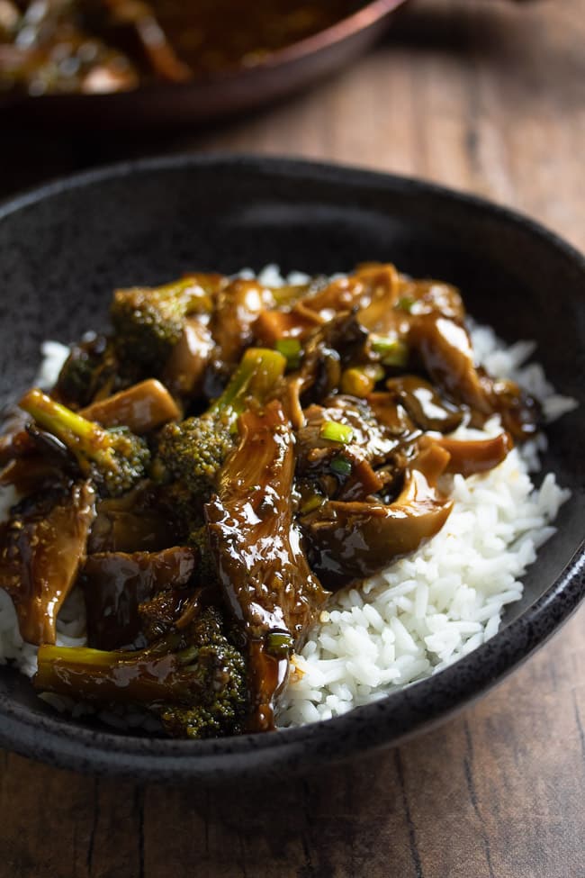 teriyaki oyster mushrooms and broccoli  over white rice in a black bowl
