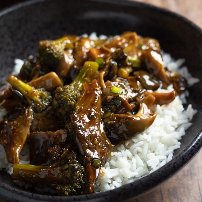 teriyaki oyster mushrooms and broccoli over white rice in a black bowl