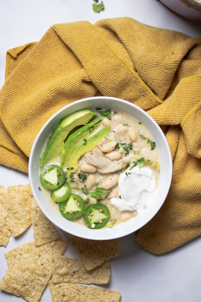 white chili in a white bowl topped with avocado slices, jalapeno slices, and vegan sour cream