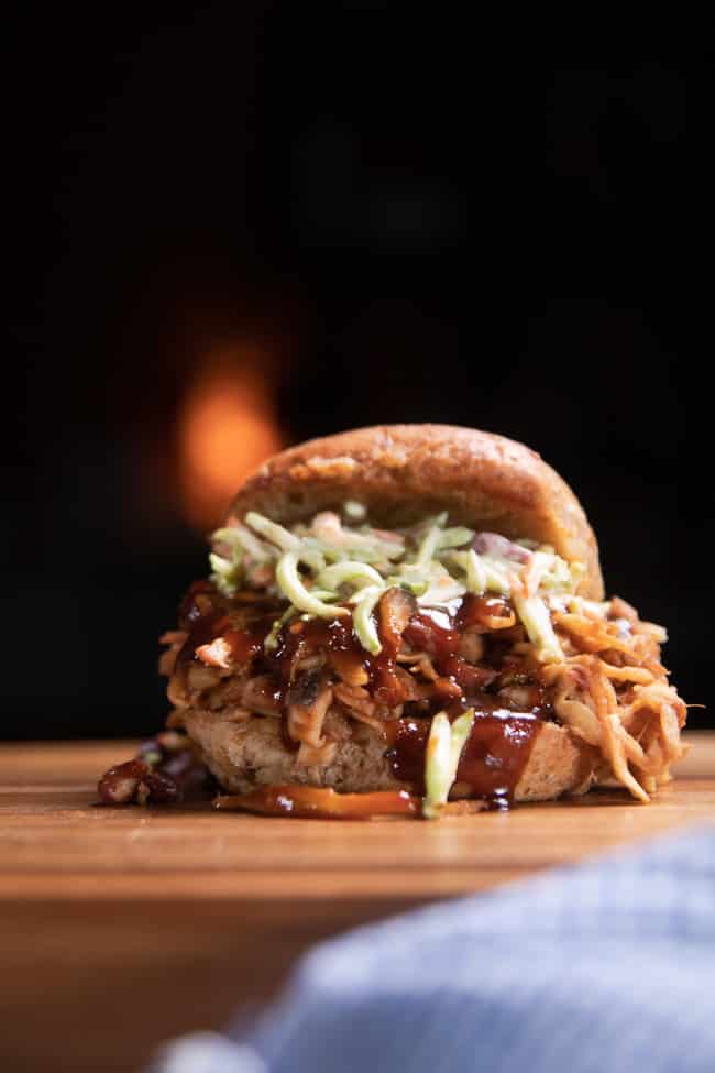 pulled pork sandwich on a cutting board topped with coleslaw