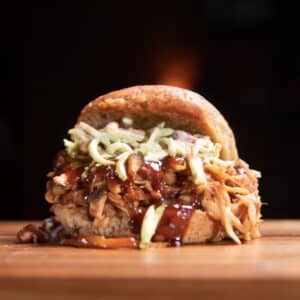 pulled pork sandwich on a cutting board topped with coleslaw
