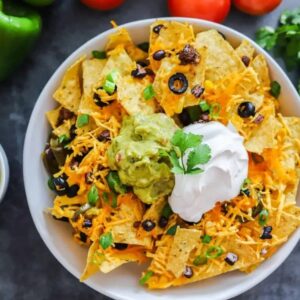vegan nachos on a white plate topped with guacamole and vegan sour cream