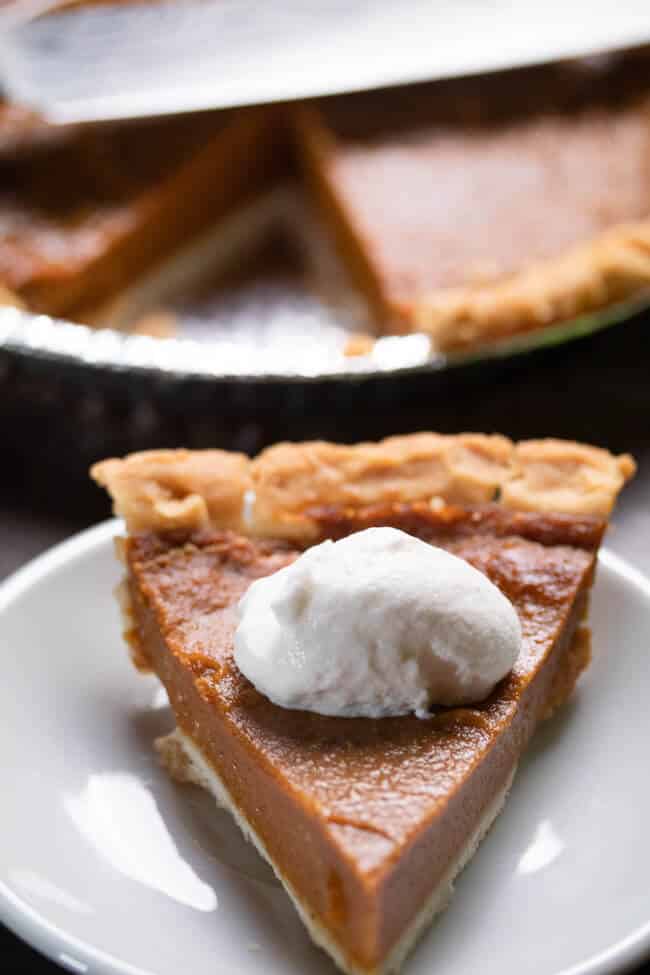 close up shot of pumpkin pie on white plate with whip cream on top