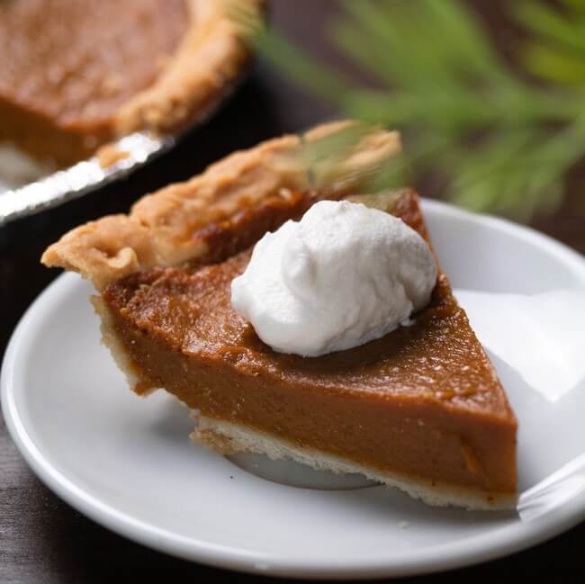 side angle view of pumpkin pie on a white plate with whip cream on top