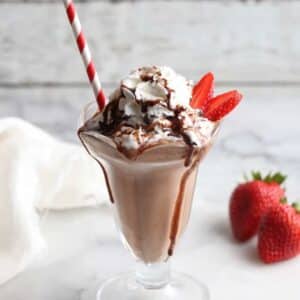 chocolate milkshake in a milkshake glass topped with whipped cream and fresh strawberries