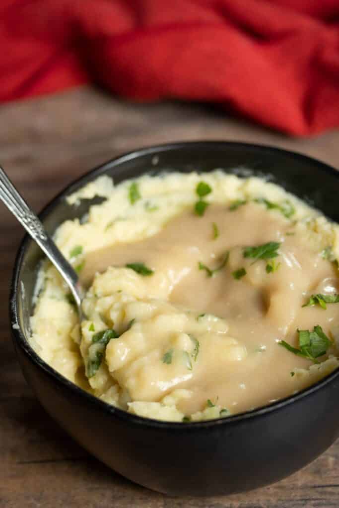 mashed potatoes with gravy on top in a black bowl with a spoon