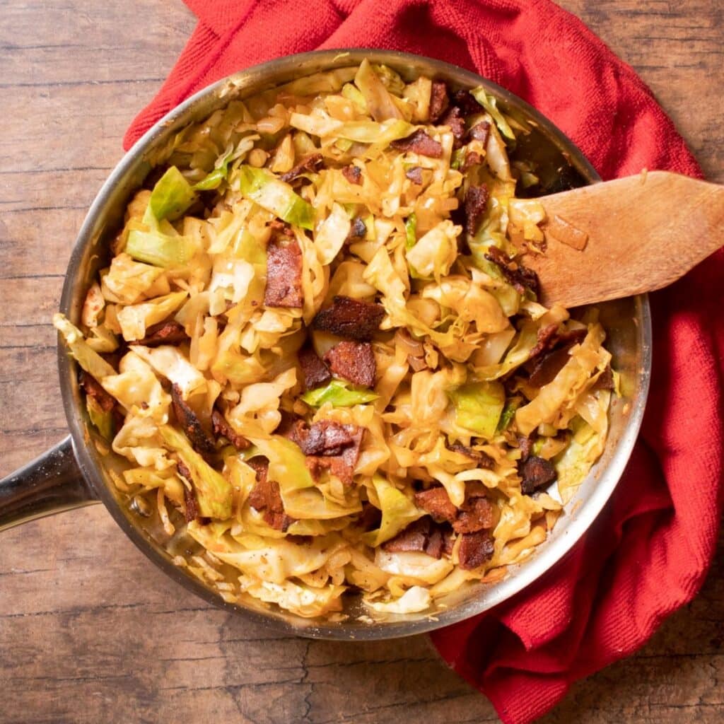 Top angle of fried cabbage in a skillet with a red towel