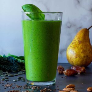 Green smoothie in a glass surrounded by flaxseed and almonds