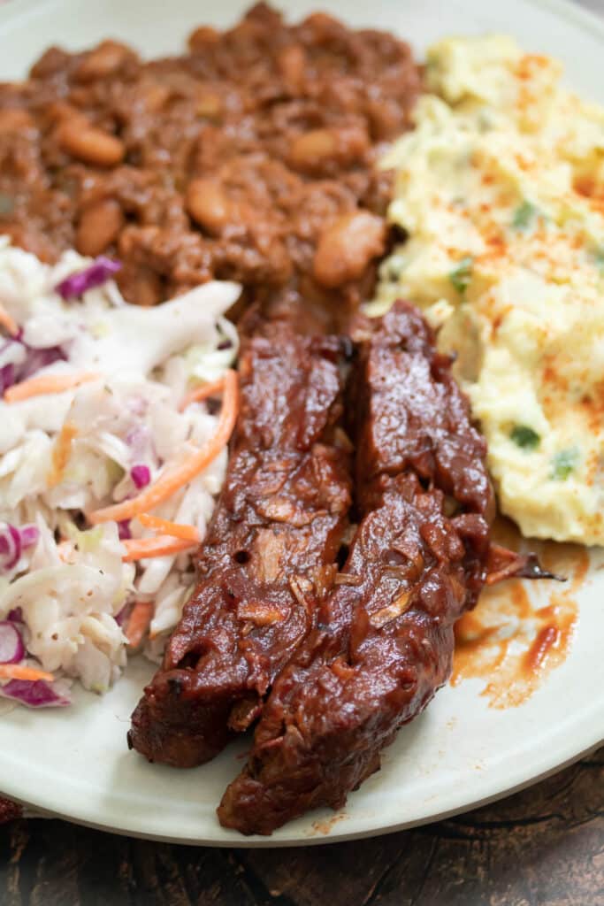 a bbq plate of food with ribs, colewslaw, potato salad, and baked beans