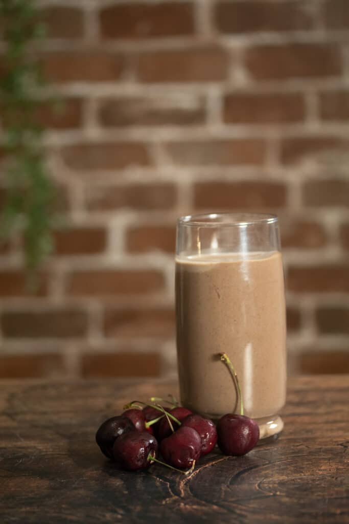 chocolate smoothie in a glass next to dark cherries