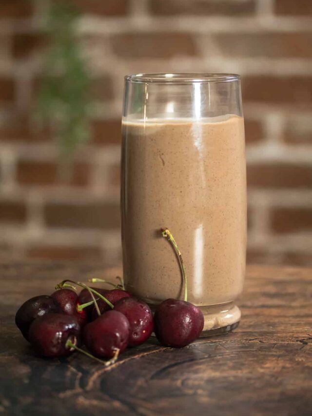 chocolate smoothie in a glass next to dark cherries