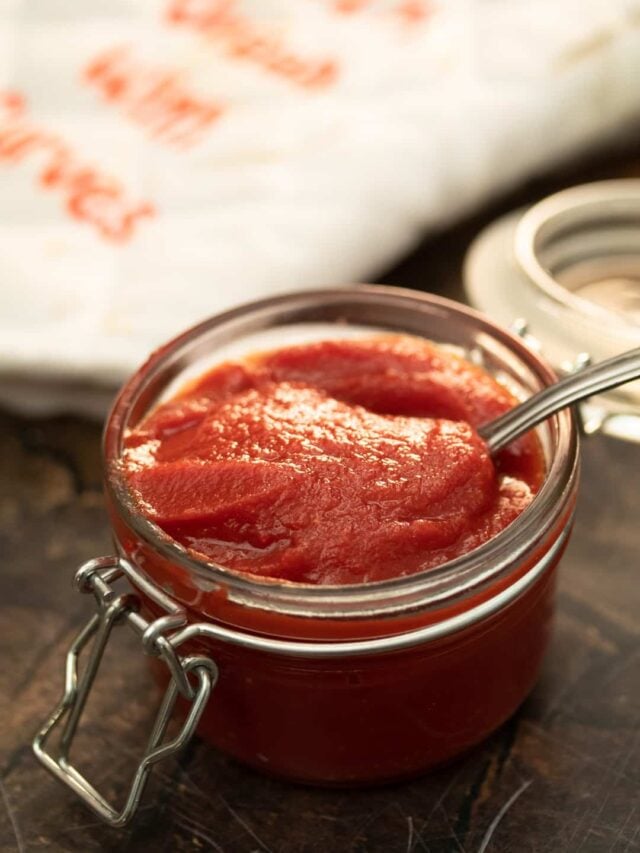 tomato paste in a glass jar with a spoon dipped into it