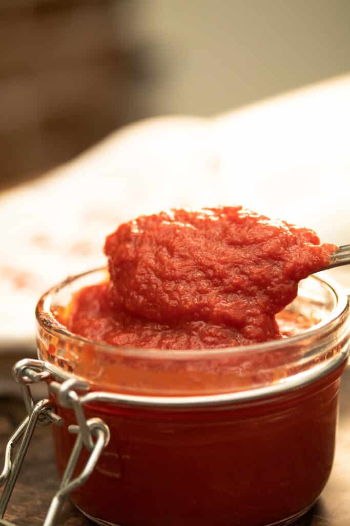 tomato paste in a glass jar with a spoons scooping out the tomato paste