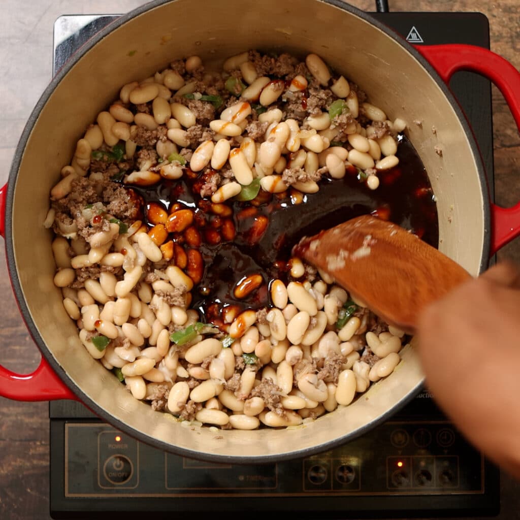 sauce and white beans in a Dutch oven being stirred together.