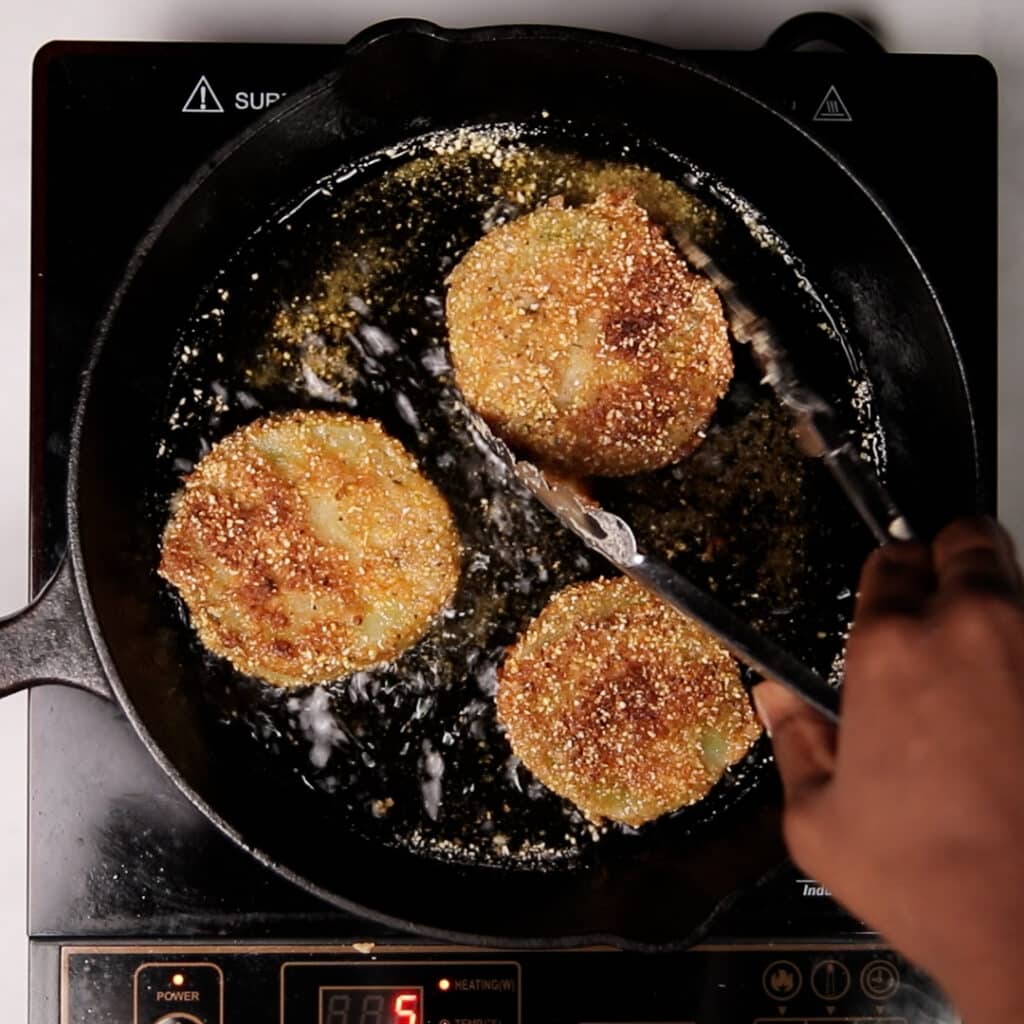green fried tomatoes being fried in oil in a cast iron