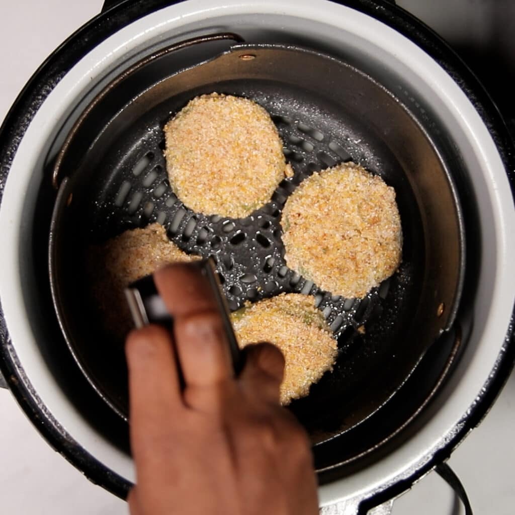 slice green tomatoes in an air fryer being sprayed with oil