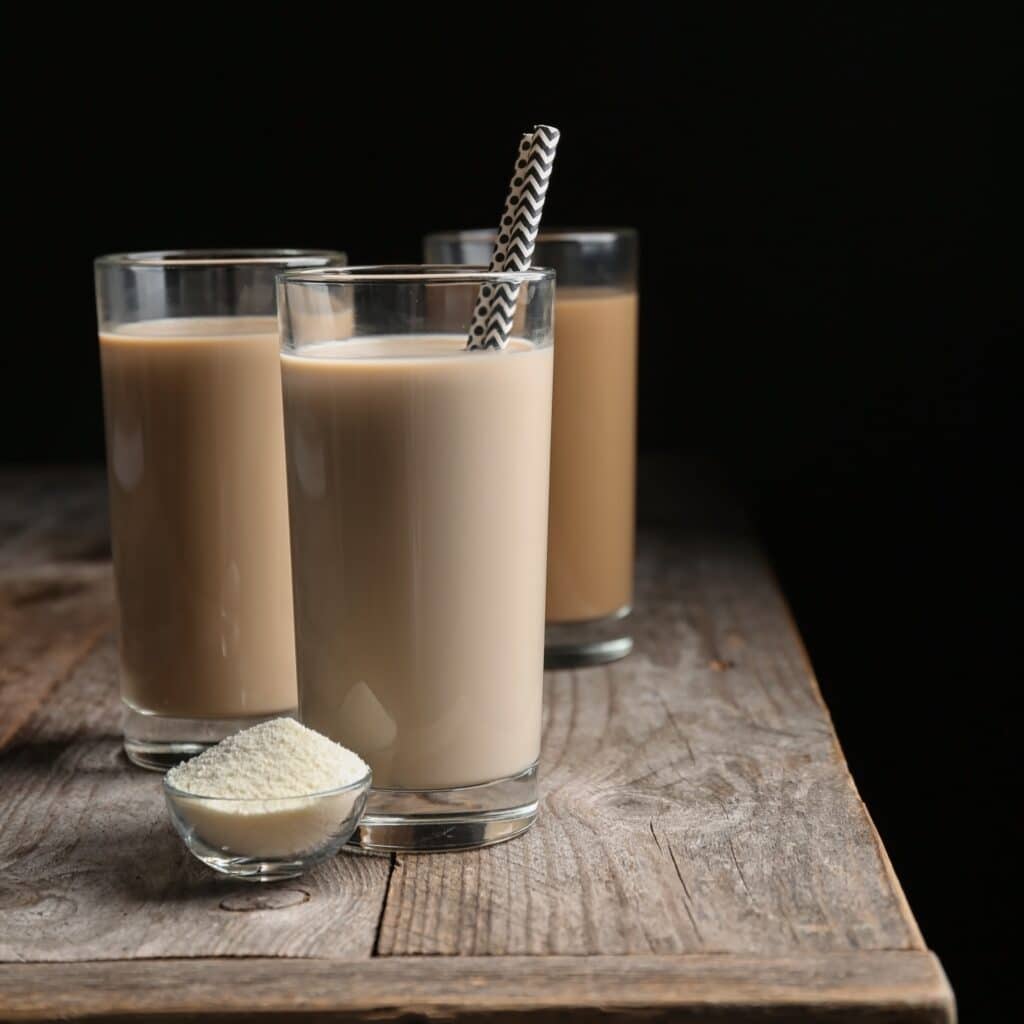 Glasses with protein shakes and powder in bowl on table against black background
