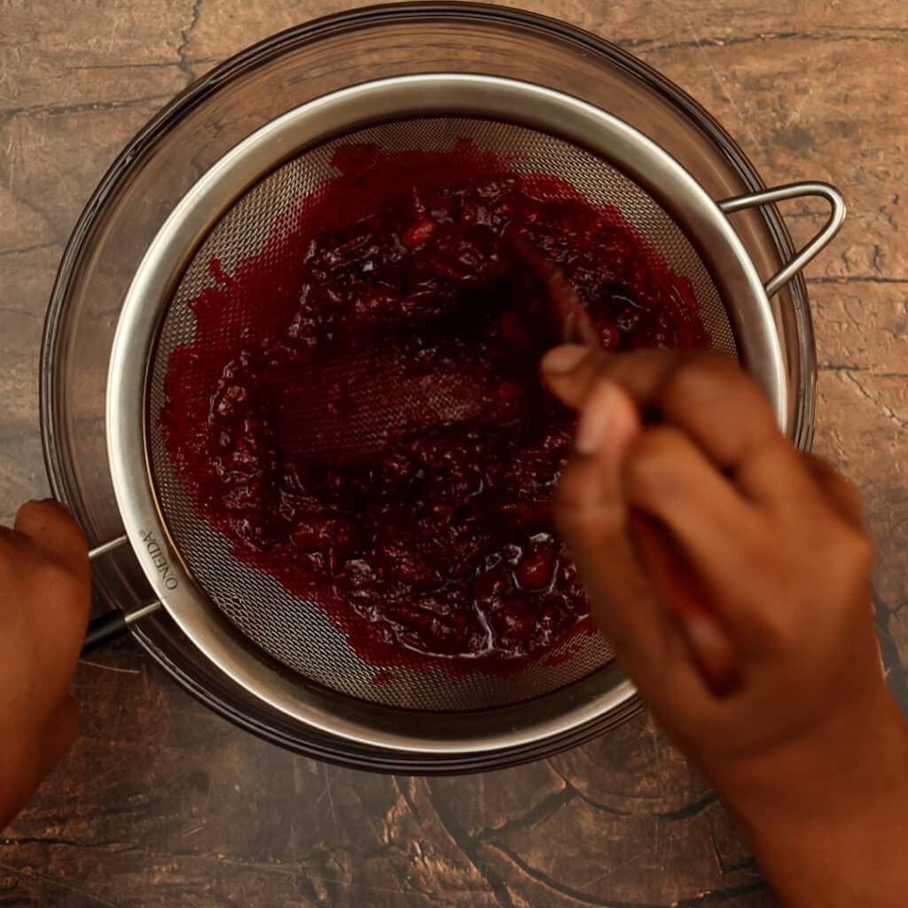 cranberry sauce being strained through mesh strainer