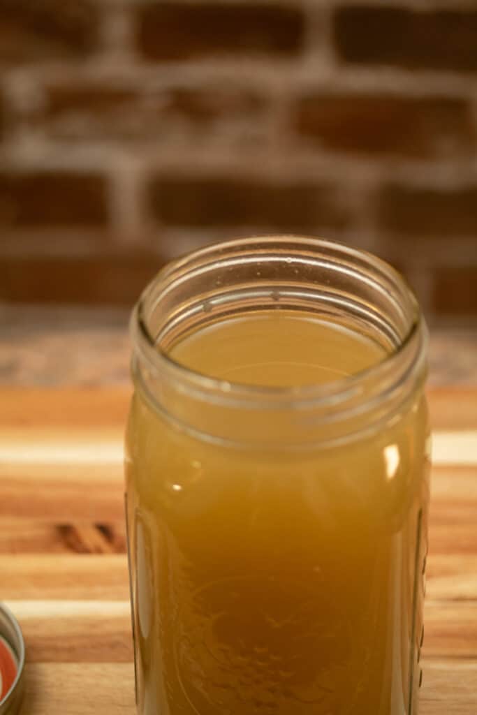 open mason jar on cutting board with broth inside of it