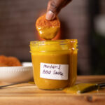 vegan nugget being dipped into mustard BBQ sauce